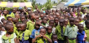 Volunteers assist a senior adult in a wheelchair by distributing aid packages outdoors.